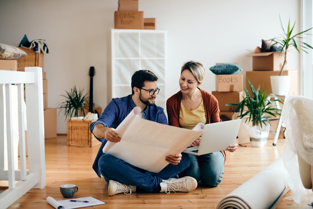 Um casal feliz a examinar planos e a usar um portátil no seu novo apartamento