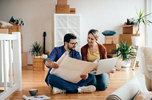 Um casal feliz a examinar planos e a usar um portátil no seu novo apartamento (Foto: Magnific)